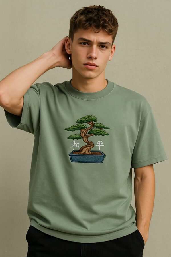 Man wearing a men's green embroidered oversized t-shirt with a bonsai tree design.